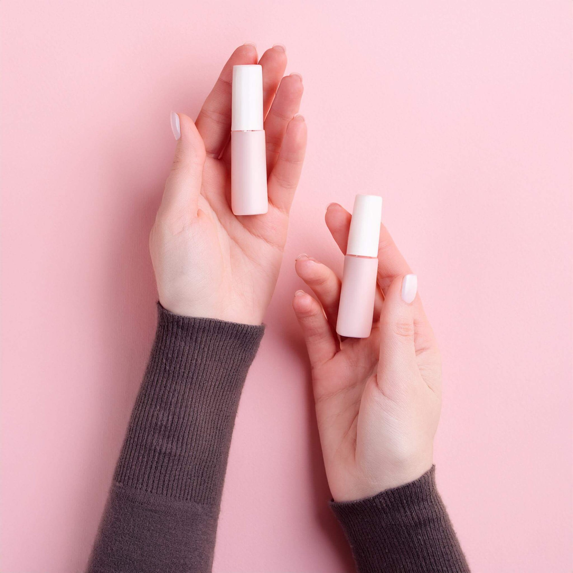 A bird's-eye view of hands holding two small lip balms.