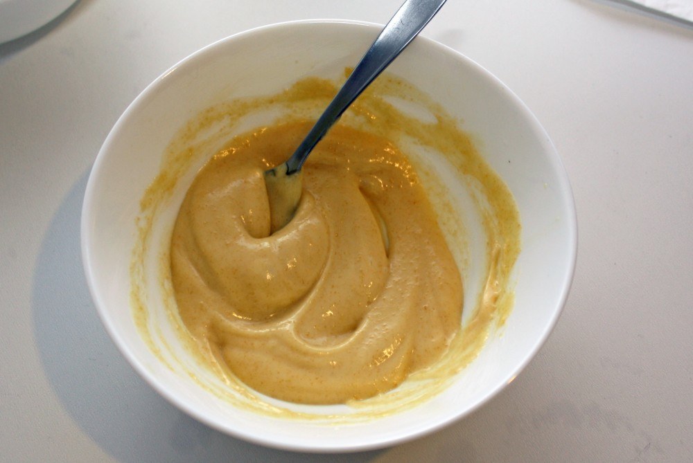 Stirring the finished day cream with a spoon in a white bowl.