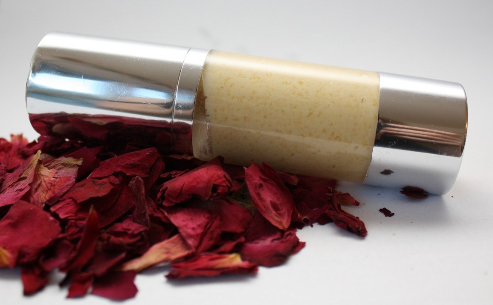 The finished day cream in a silver airless bottle resting on dried rose petals.