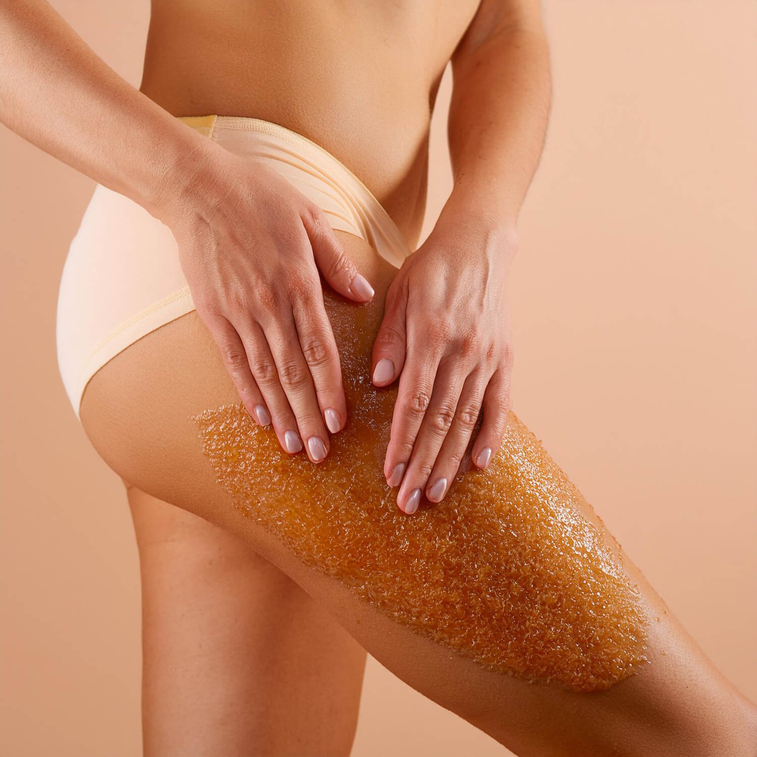 Gel body scrub in a large clear glass jar, containing glitter, some of which has been scooped up on a small plastic scoop.
