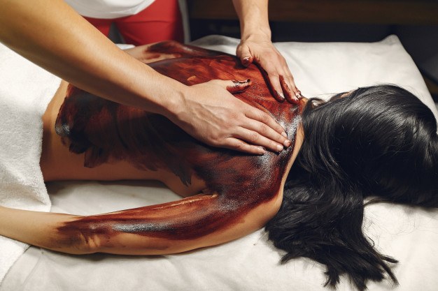 A body mask made of cosmetic clay applied to the back of a woman lying on a massage table.