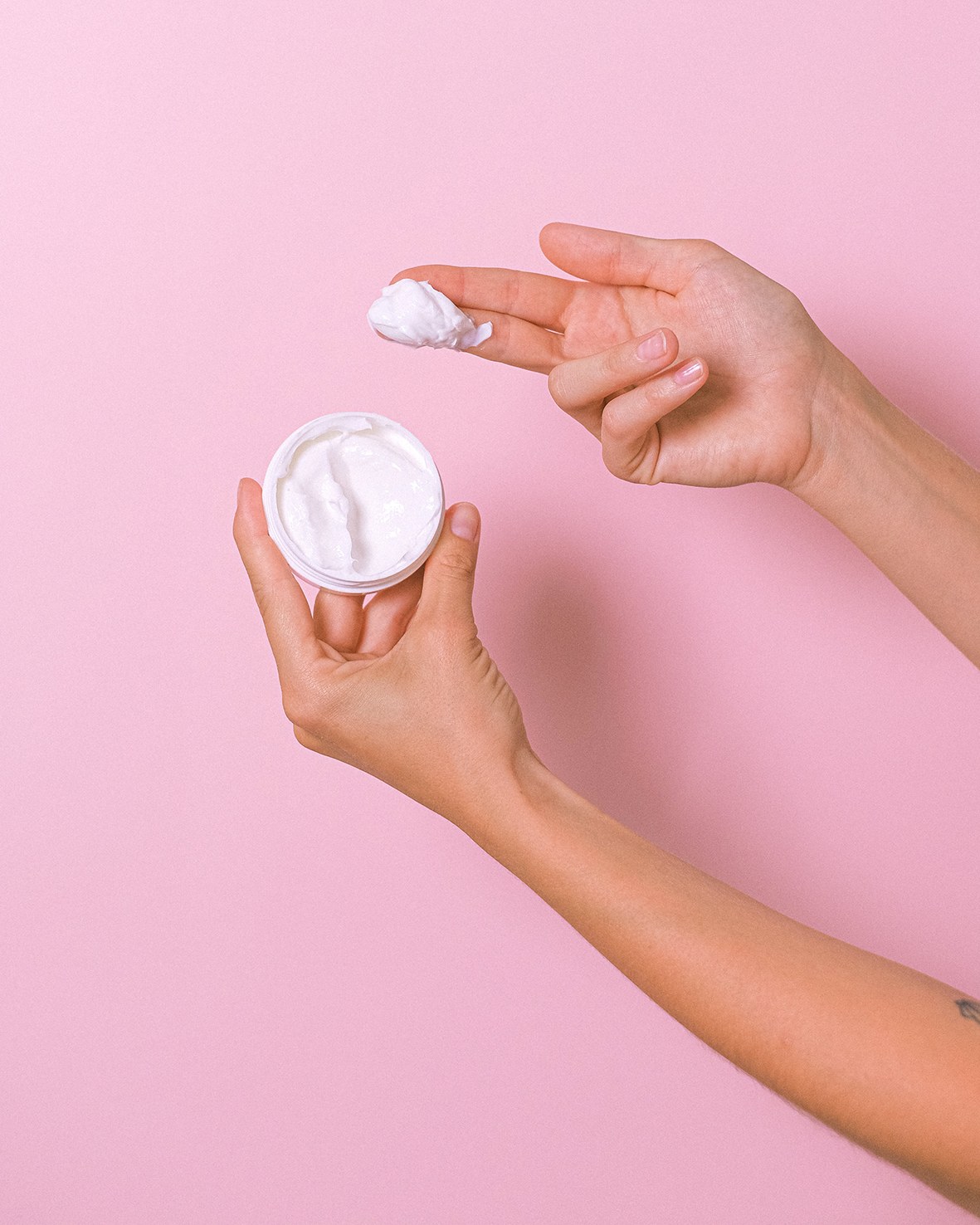 Une femme applique sur ses mains du beurre corporel hydratant contenu dans un pot en plastique.