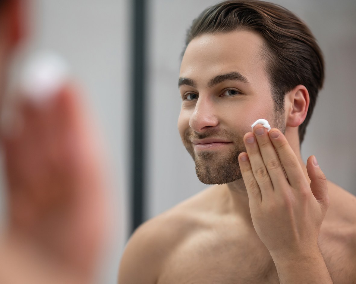 Un homme se tient devant un miroir et applique sur son visage le sérum visage et barbe.