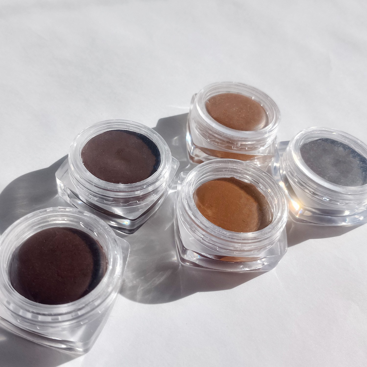 Cires pour sourcils à base de matières premières naturelles, de différentes couleurs, dans de petits pots transparents sur fond blanc. Fabriquez-les selon le tutoriel Handymade.